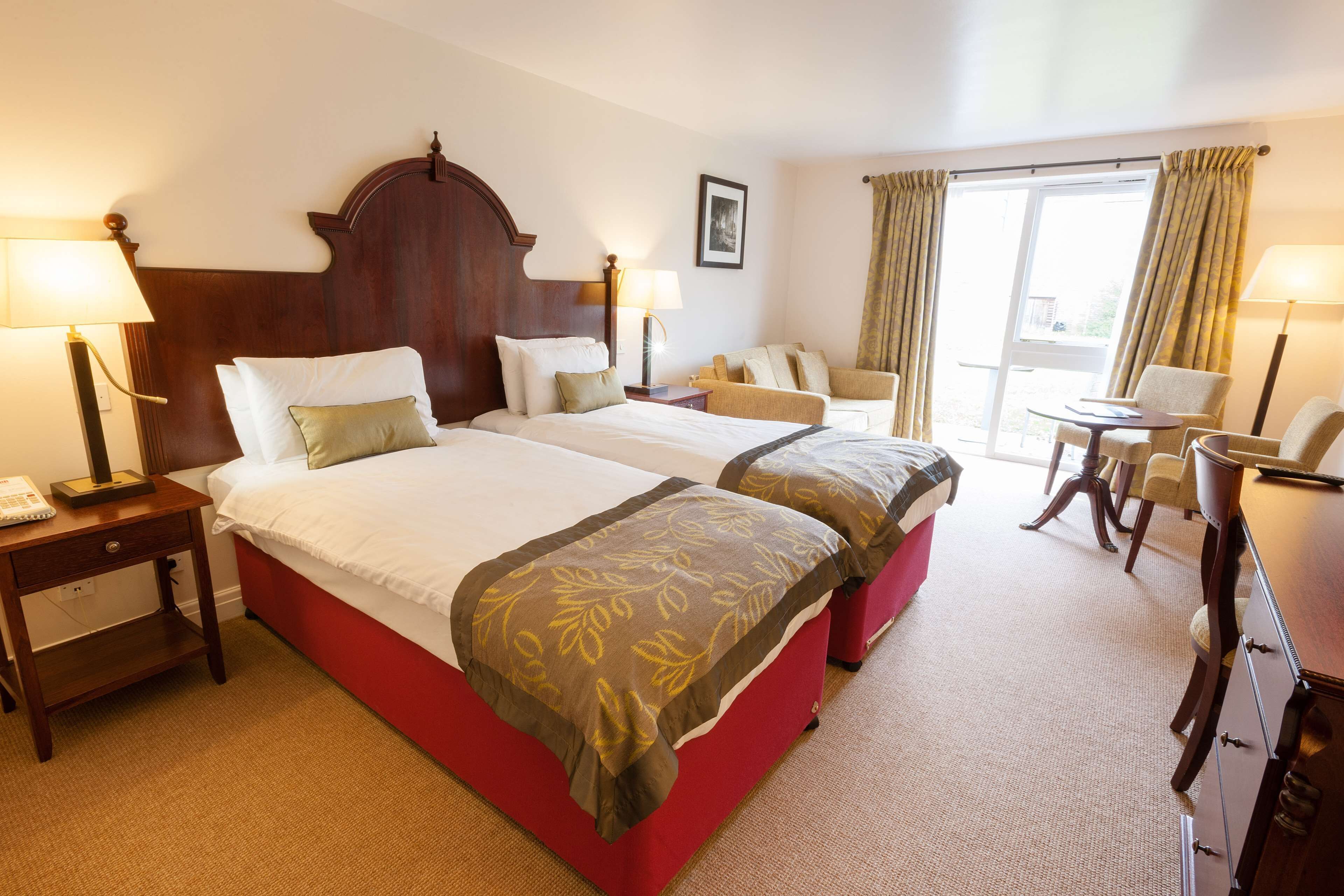 A hotel room with two beds, a desk, a chair, and a small table.