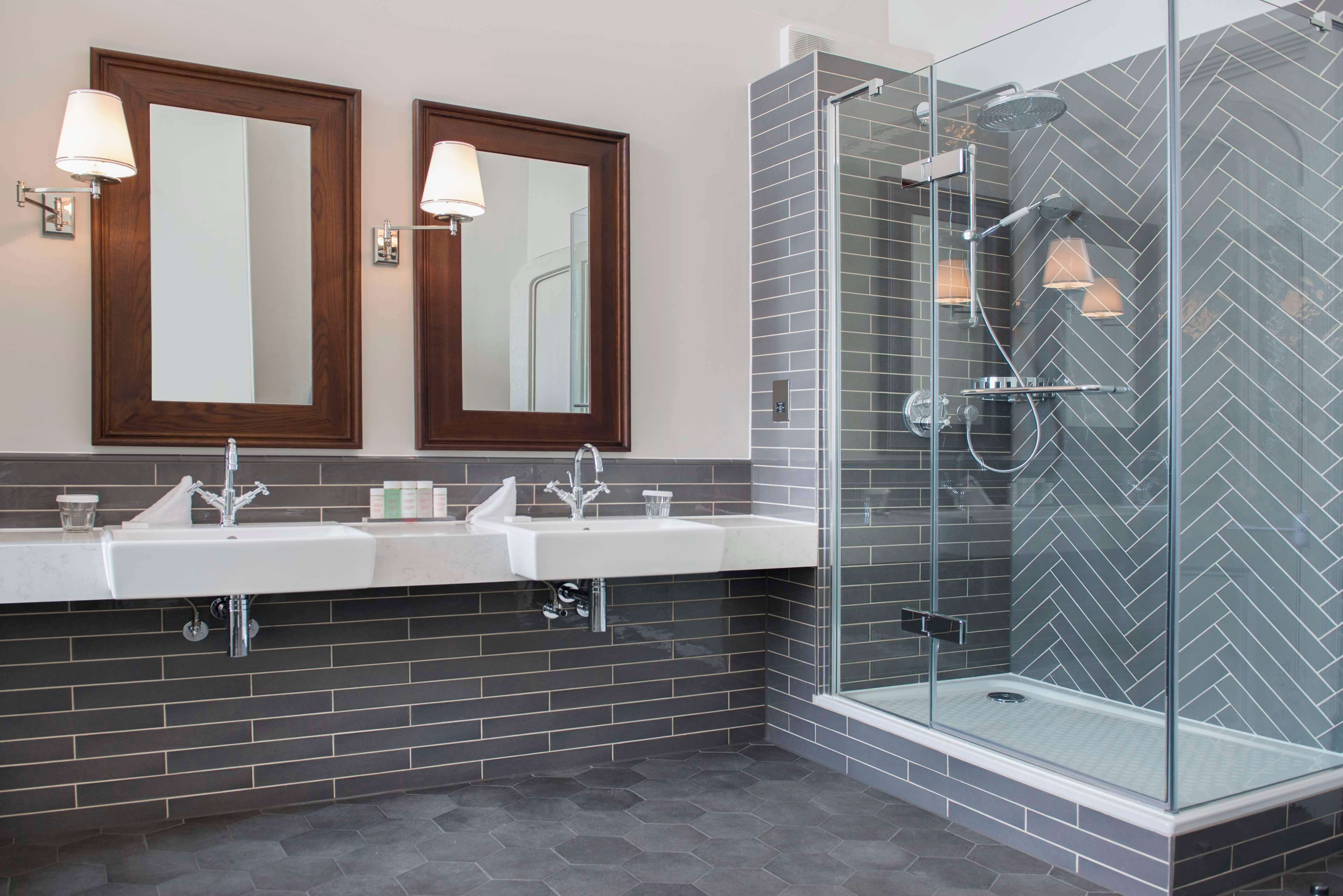 A modern bathroom with two sinks, a glass shower enclosure, and wooden-framed mirrors.