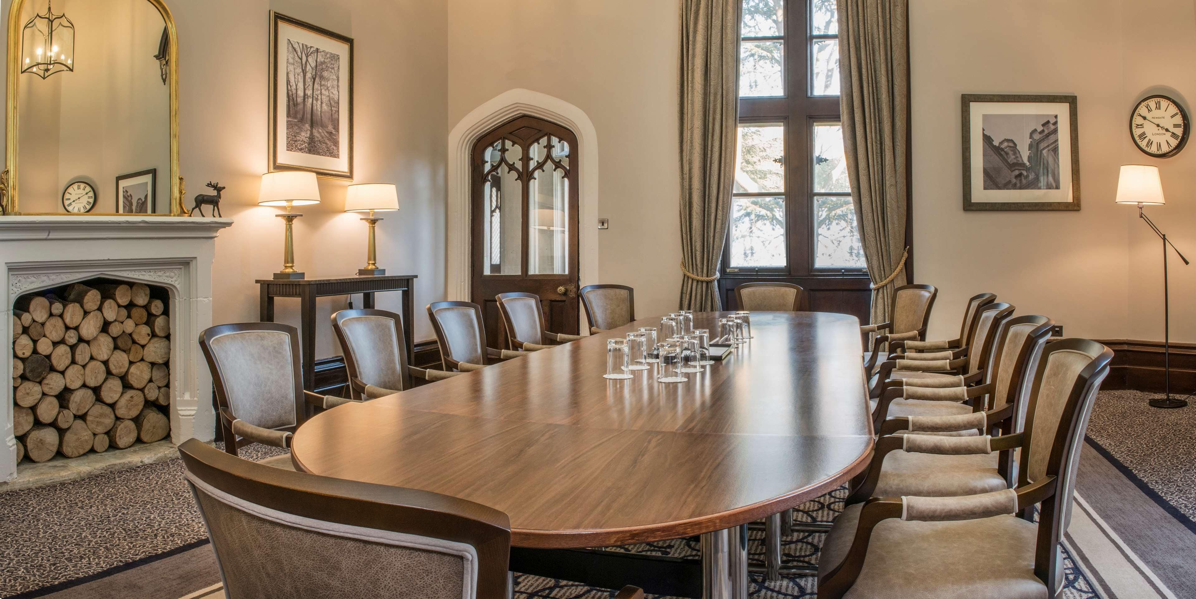 A conference room with a long table, chairs, a fireplace, and framed pictures on the walls.