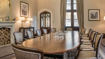 A conference room with a long table, chairs, a fireplace, and framed pictures on the walls.