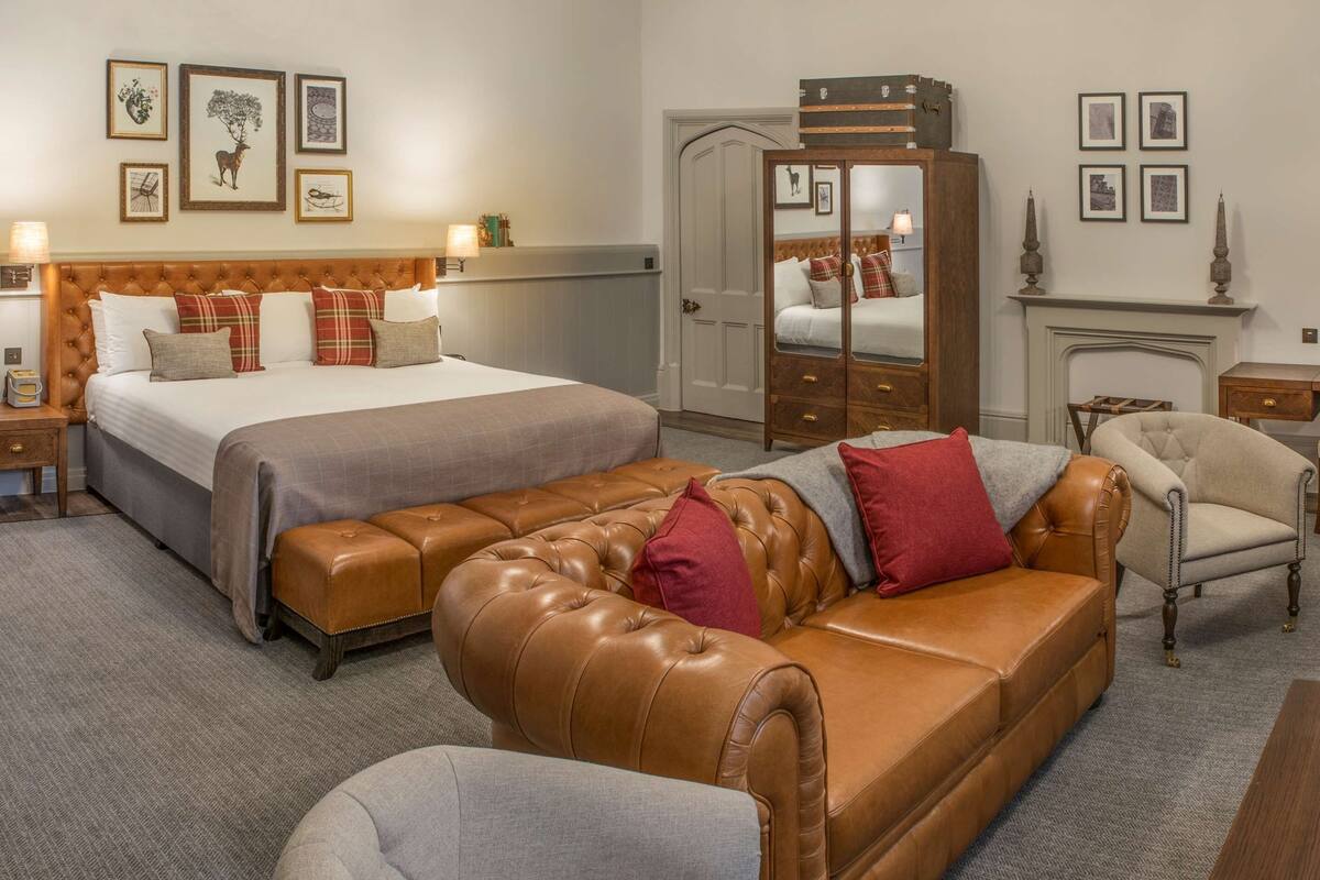 Een hotelkamer met een groot bed, een leren bank, een houten garderobe en een bureau met stoel.