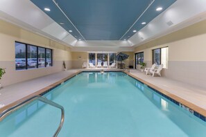 Una piscina interior con agua azul cristalina, rodeada de sillones blancos y un techo con iluminación empotrada.