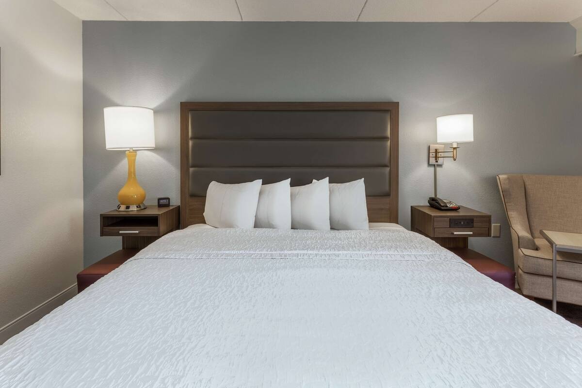 Habitación de hotel con una cama grande, dos mesitas de noche con lámparas, una silla y un buró con teléfono.