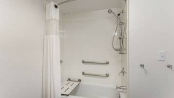 Un baño moderno con cabina de ducha, barras de apoyo y una bañera blanca.