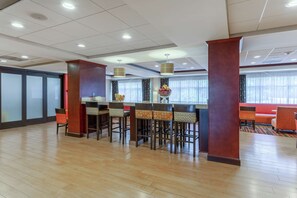 A hotel lobby with a bar area, wooden flooring, and a seating area with orange chairs.