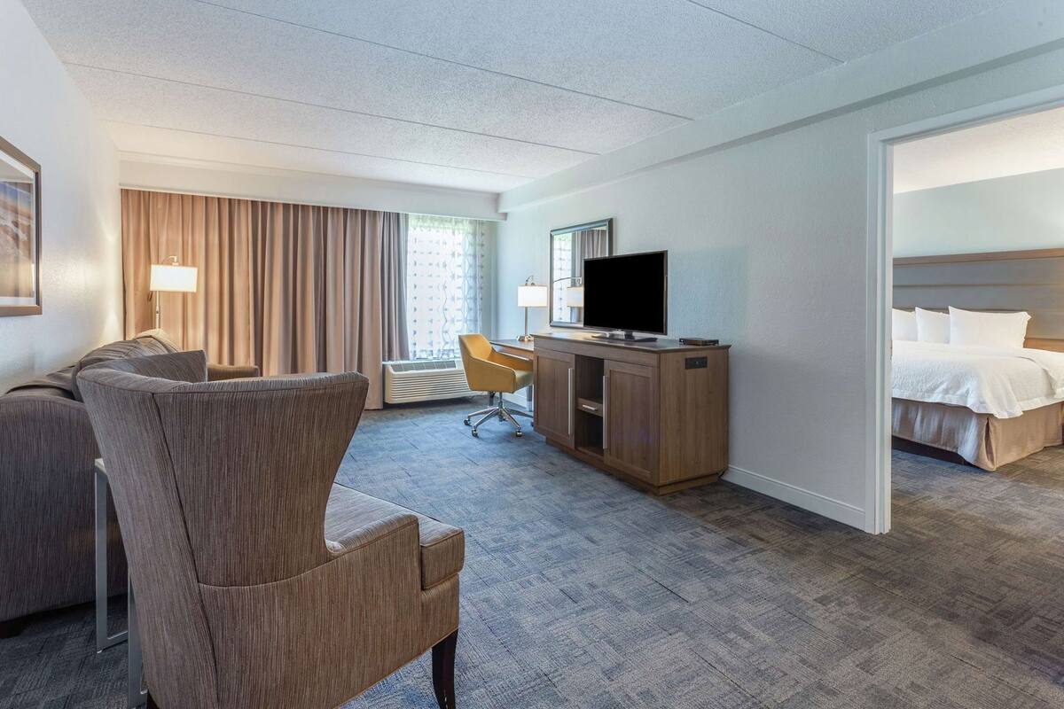 Una habitación de hotel con sofá, escritorio con televisor, cama y ventana con cortinas.