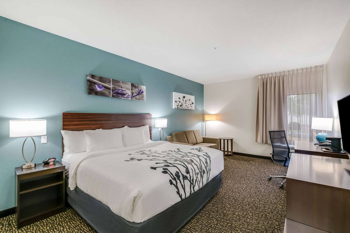 A hotel room with a bed, bedside tables, a desk, a chair, and artwork on the walls.