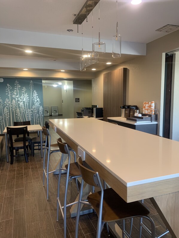 A modern bar area with a long counter, metal stools, and pendant lighting.