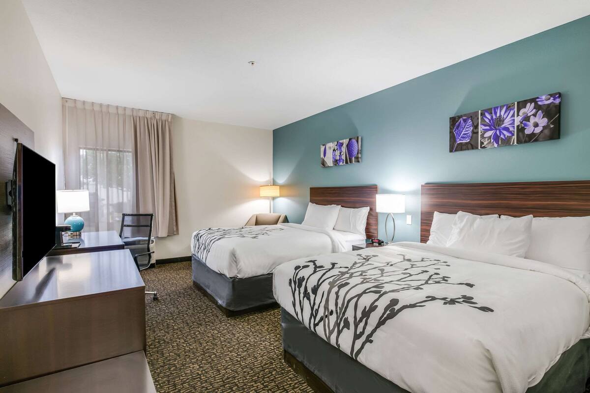A hotel room with two beds, a desk, a TV, and artwork on the walls.