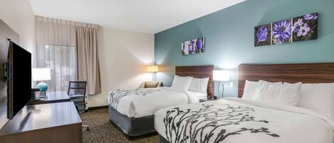 A hotel room with two beds, a desk, a TV, and artwork on the walls.