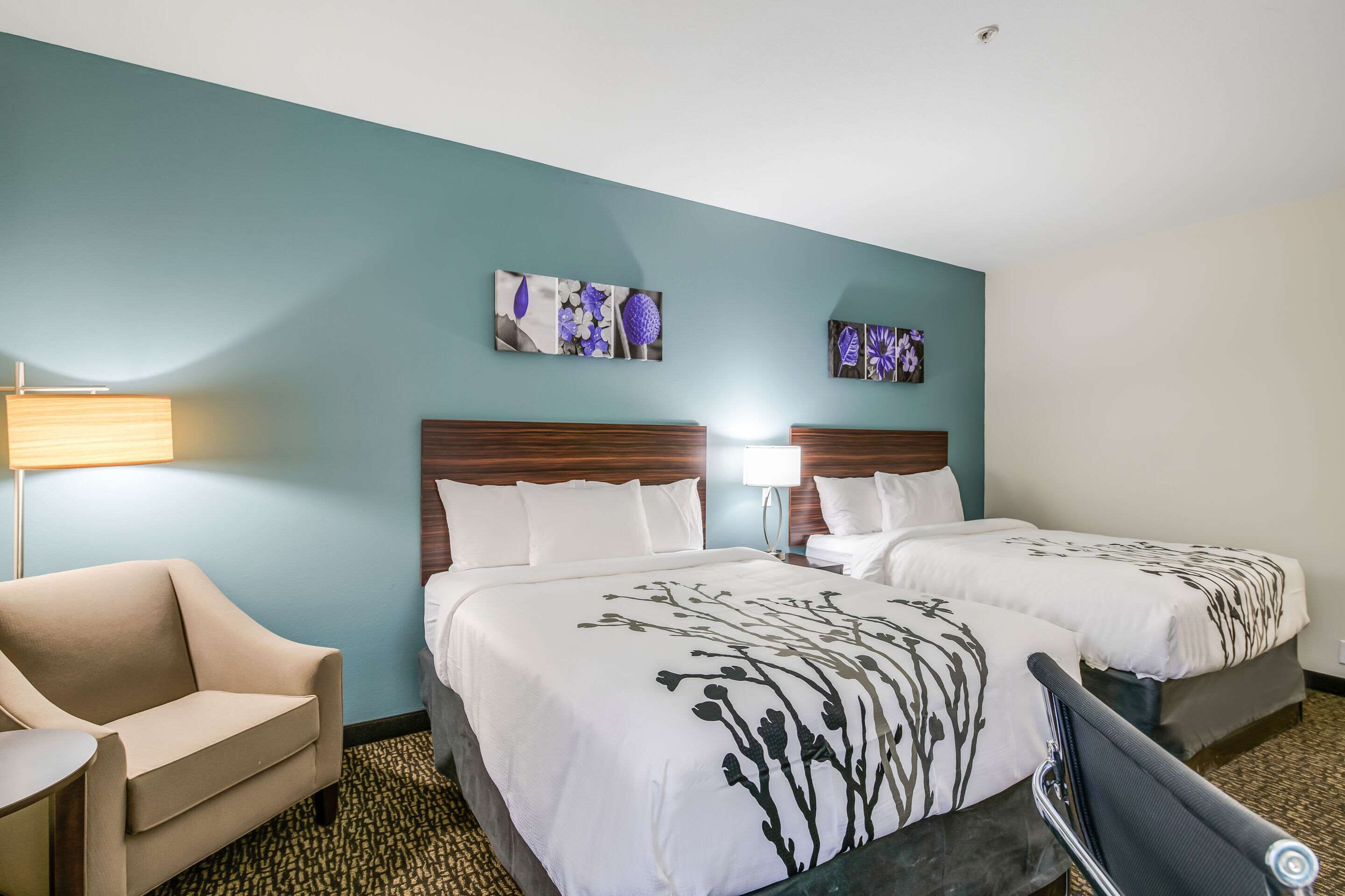 A hotel room with two beds, a sofa, a lamp, and artwork on the walls.