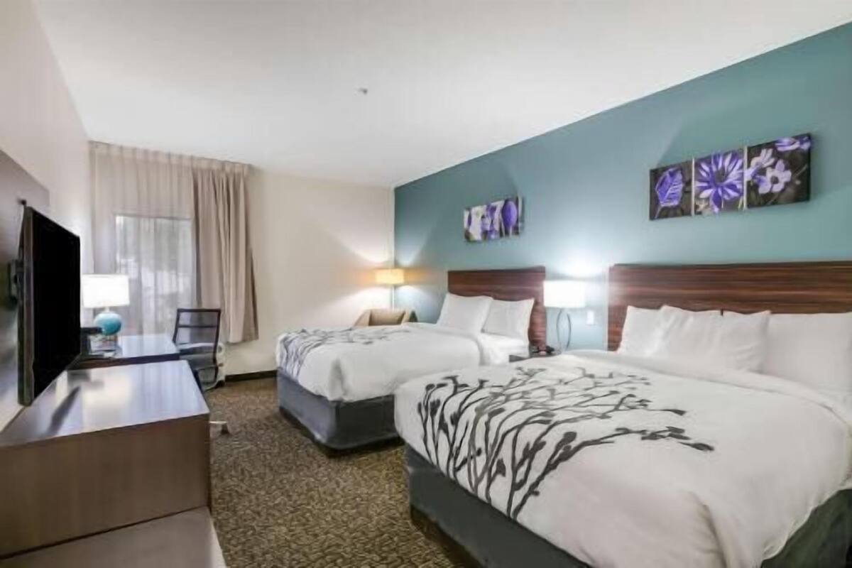 A hotel room with two beds, a desk, a TV, and artwork on the wall.