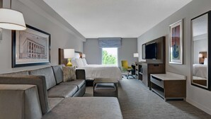 Une chambre d’hôtel avec un grand lit, un canapé, un bureau, une télévision et une fenêtre donnant sur un paysage verdoyant.