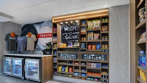 Un bar proposant des collations, avec un panneau noir accueillant les visiteurs, des étagères remplies de snacks et de boissons, et deux vitrines réfrigérées.