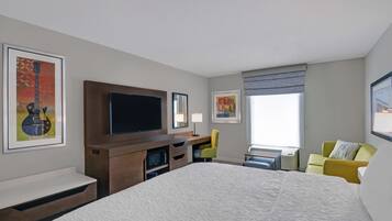 Quarto de hotel com uma cama grande, televisão de tela plana, escrivaninha com cadeira e obras de arte nas paredes.