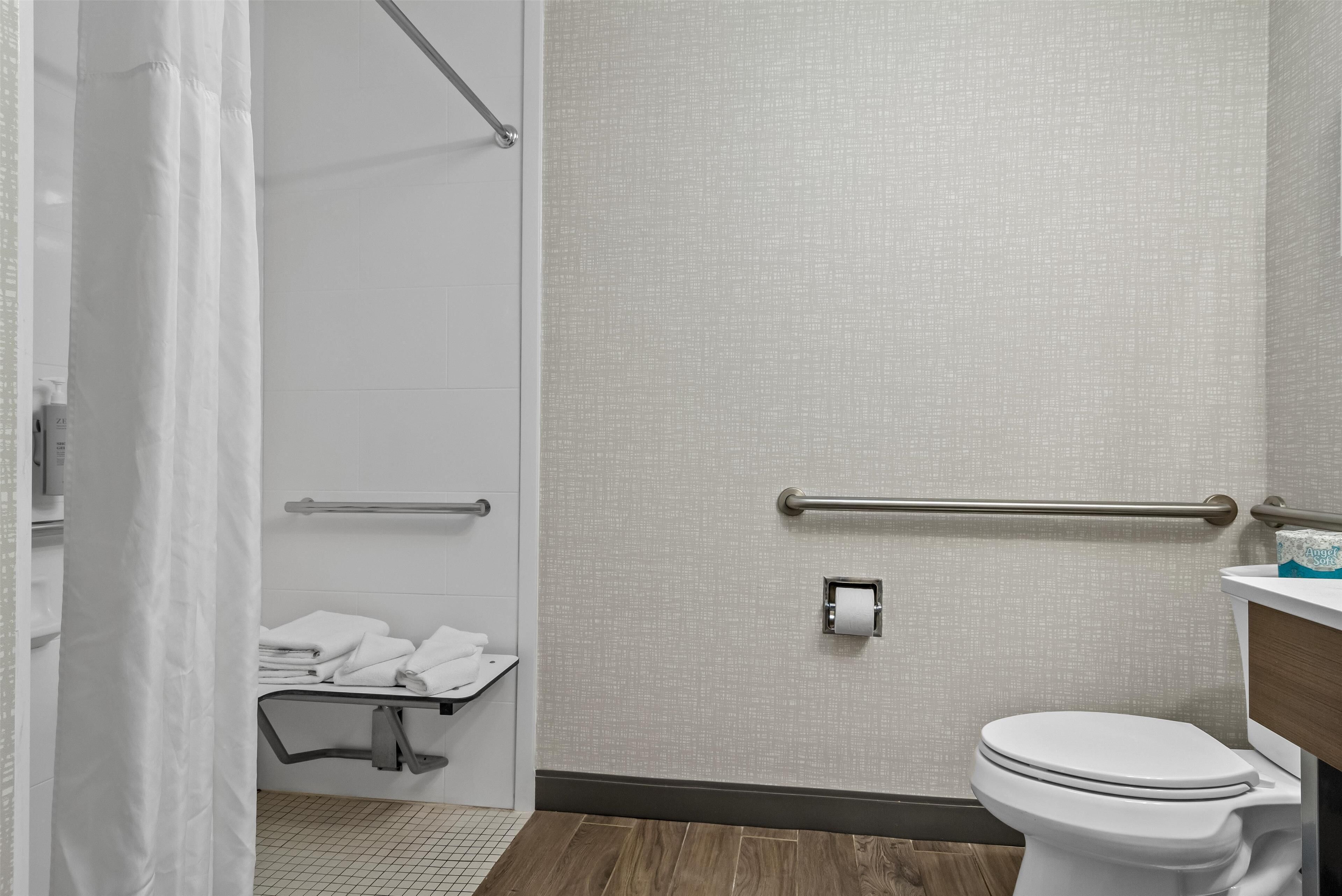 Un baño moderno con ducha, barras de apoyo, inodoro y perchero para toallas.