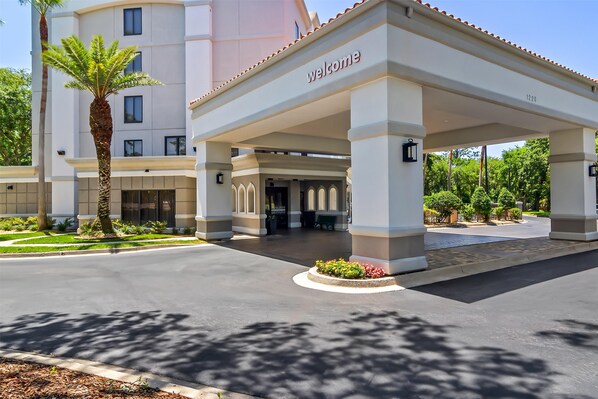 Entrada de hotel con un cartel que dice 'welcome', una palmera y un edificio con varias ventanas.