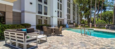 A poolside area with a white building, outdoor furniture, and a clear blue pool.