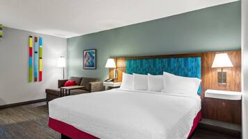 Habitación de hotel con una cama grande, dos mesitas de noche con lámparas, un sofá, una pequeña mesa y un cuadro abstracto de colores en la pared.