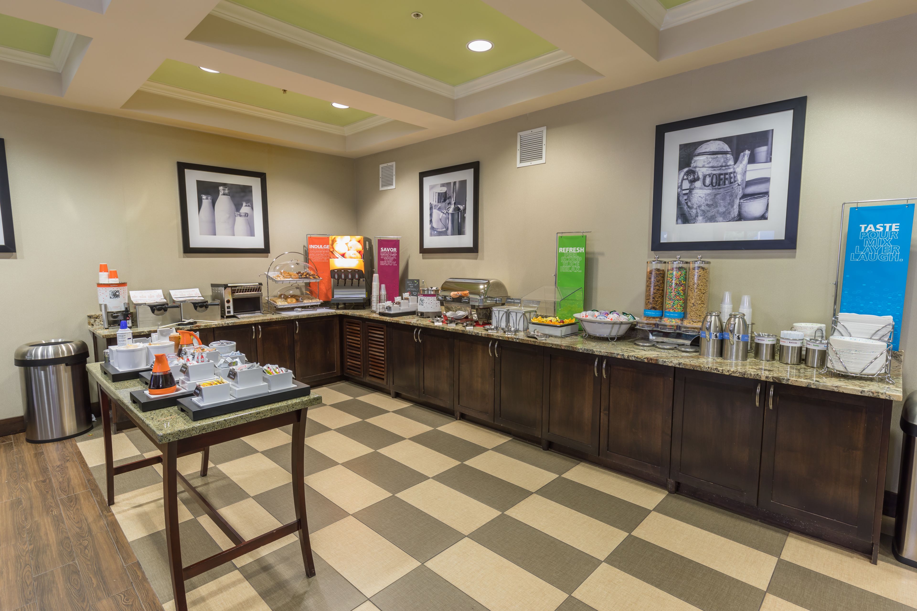 A hotel kitchen with a checkered floor, a buffet counter, and various food and beverage stations.