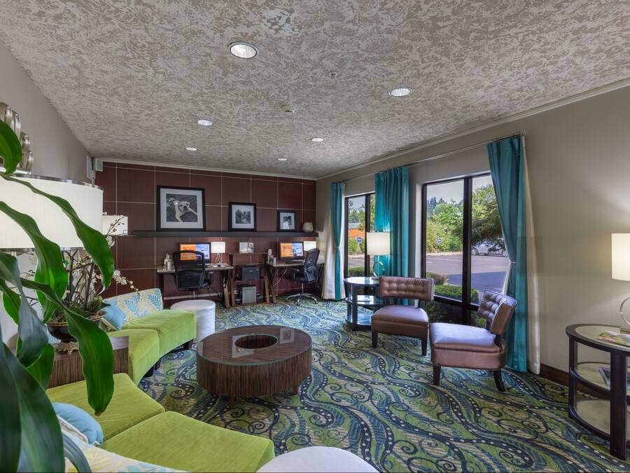 A hotel lobby with a patterned carpet, seating area with couches and chairs, a small table, and a desk with computers.