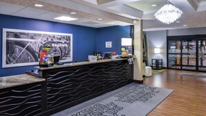 A hotel reception area with a blue wall, a large framed picture, a reception desk, and a welcome mat.