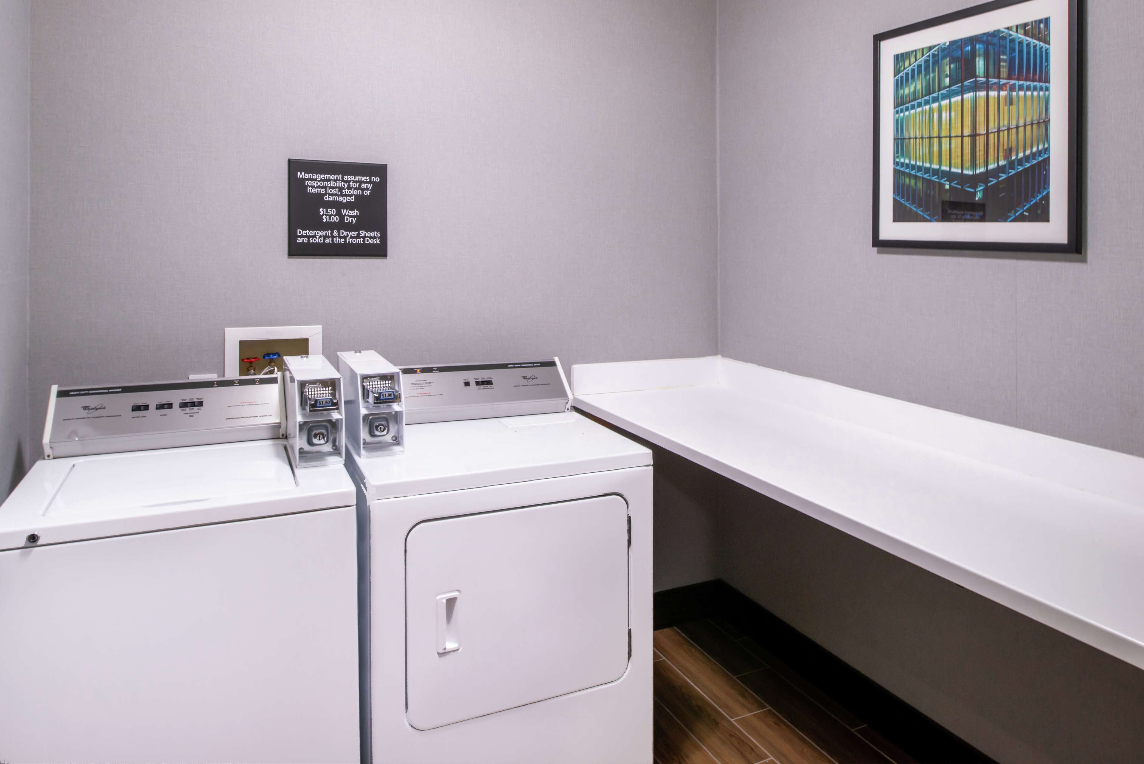 A laundry area with two front-loading washers and a drying rack. A sign indicates laundry fees.