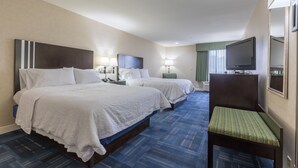 A hotel room with two beds, a desk, a chair, a television, and a window with curtains.