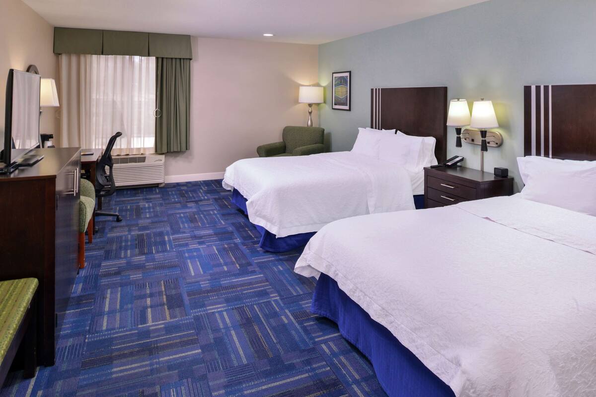 A hotel room with two beds, a desk with a chair, a lamp, and a picture on the wall.