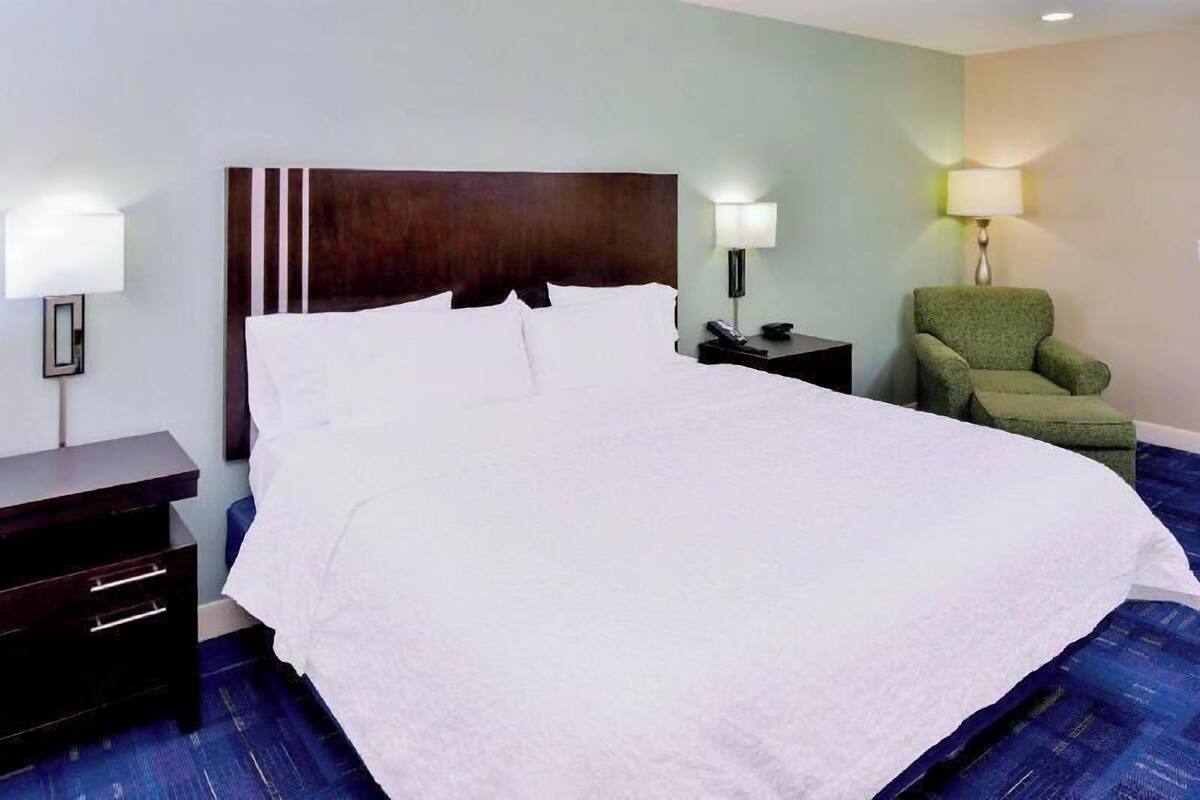 A hotel room with a large bed, two bedside tables, a green armchair, and two wall-mounted lamps.