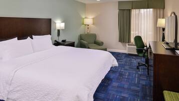 A hotel room with a large bed, a desk with a computer, a chair, a lamp, and a window with curtains.