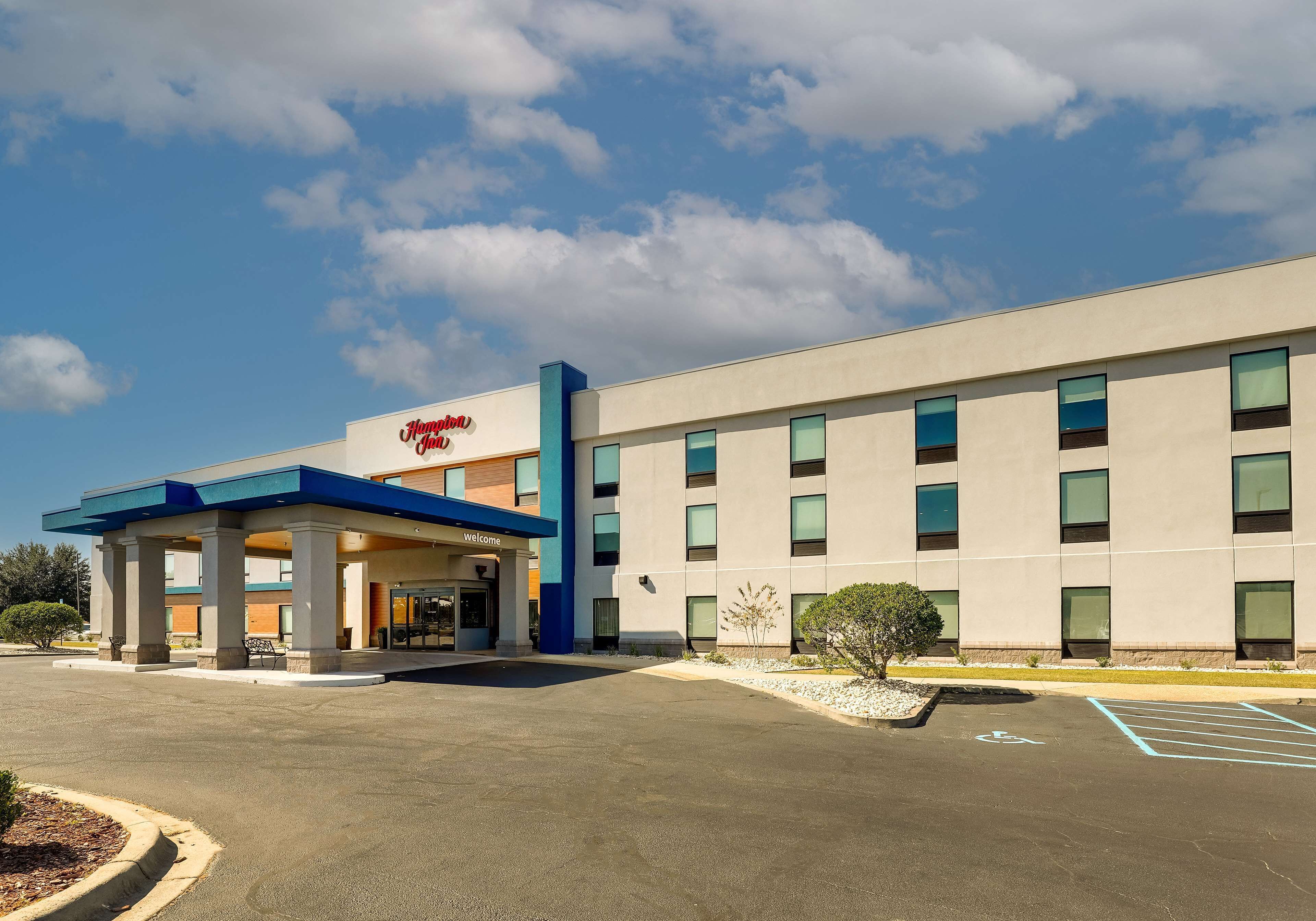 A modern hotel with a blue and white facade, a covered entrance, and a parking lot with handicapped accessibility.