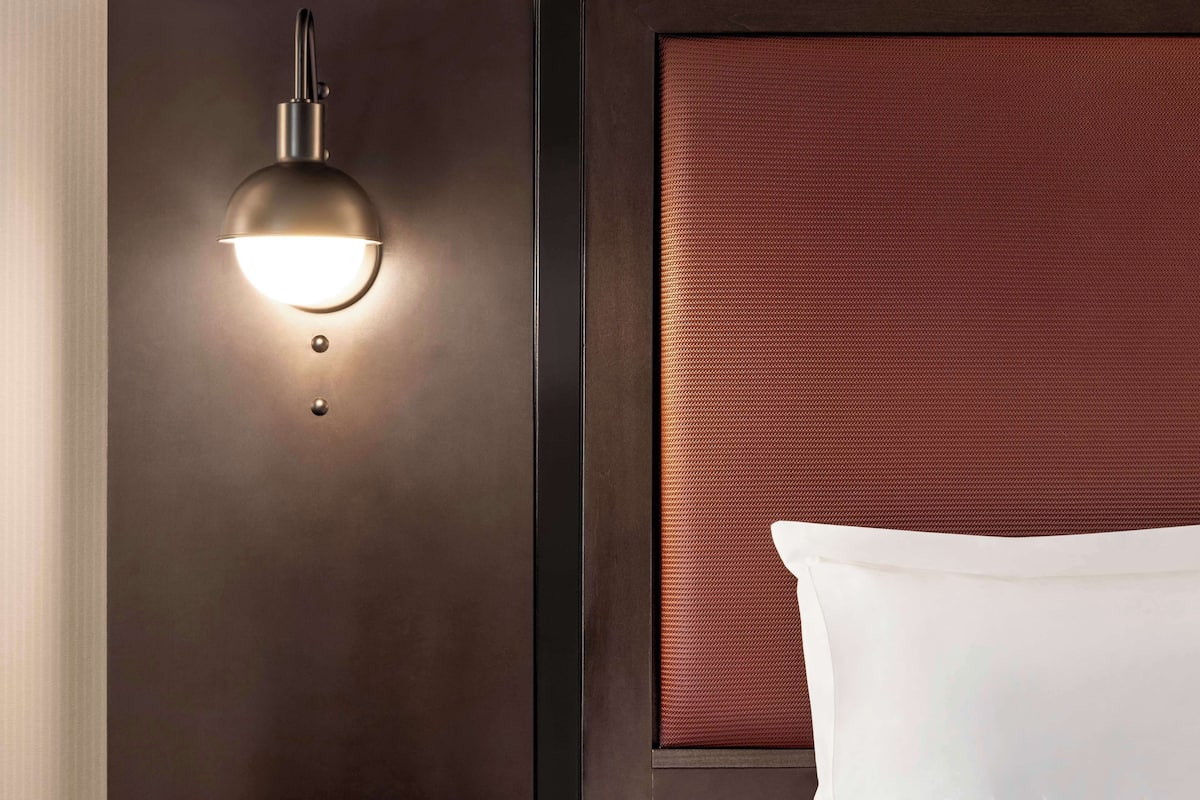 A modern room with a dark wall, a round wall-mounted light fixture, and a textured red headboard.