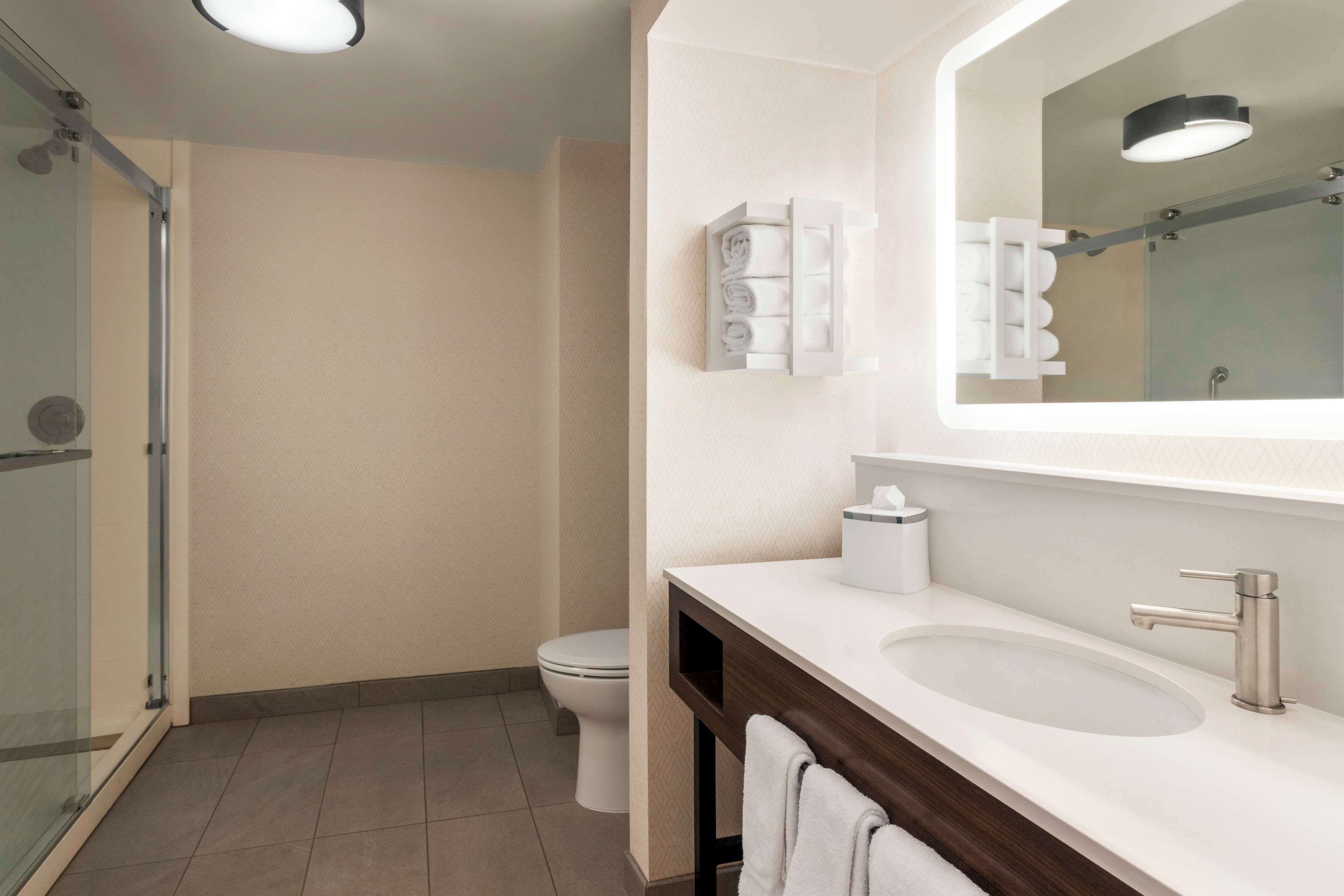 Een moderne badkamer met een glazen douchecabine, toilet, wastafel met spiegel en een handdoekhouder.