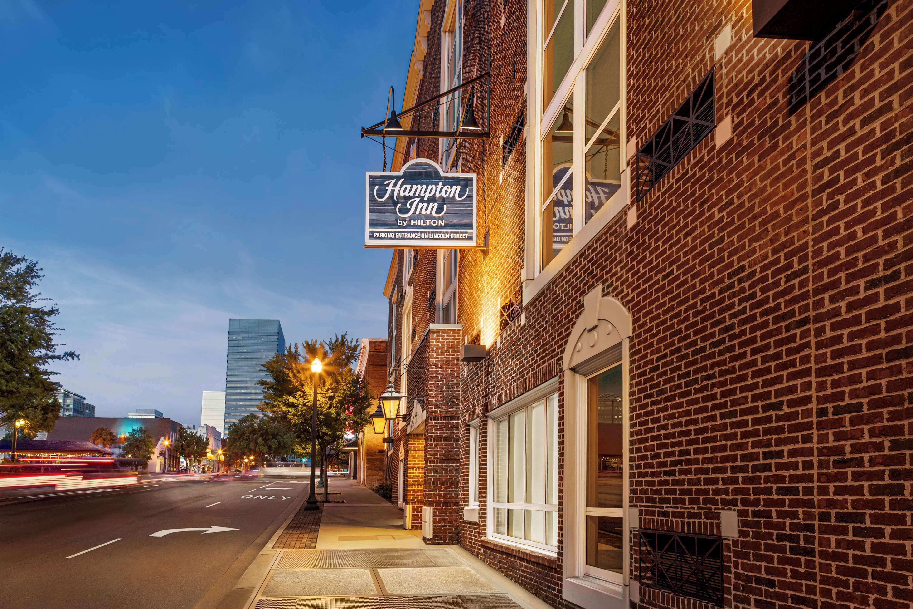 A Hampton Inn by Hilton sign on a brick building with a clear sky.