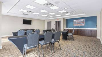 A conference room with a long table, multiple chairs, a projector screen, and a carpeted floor.
