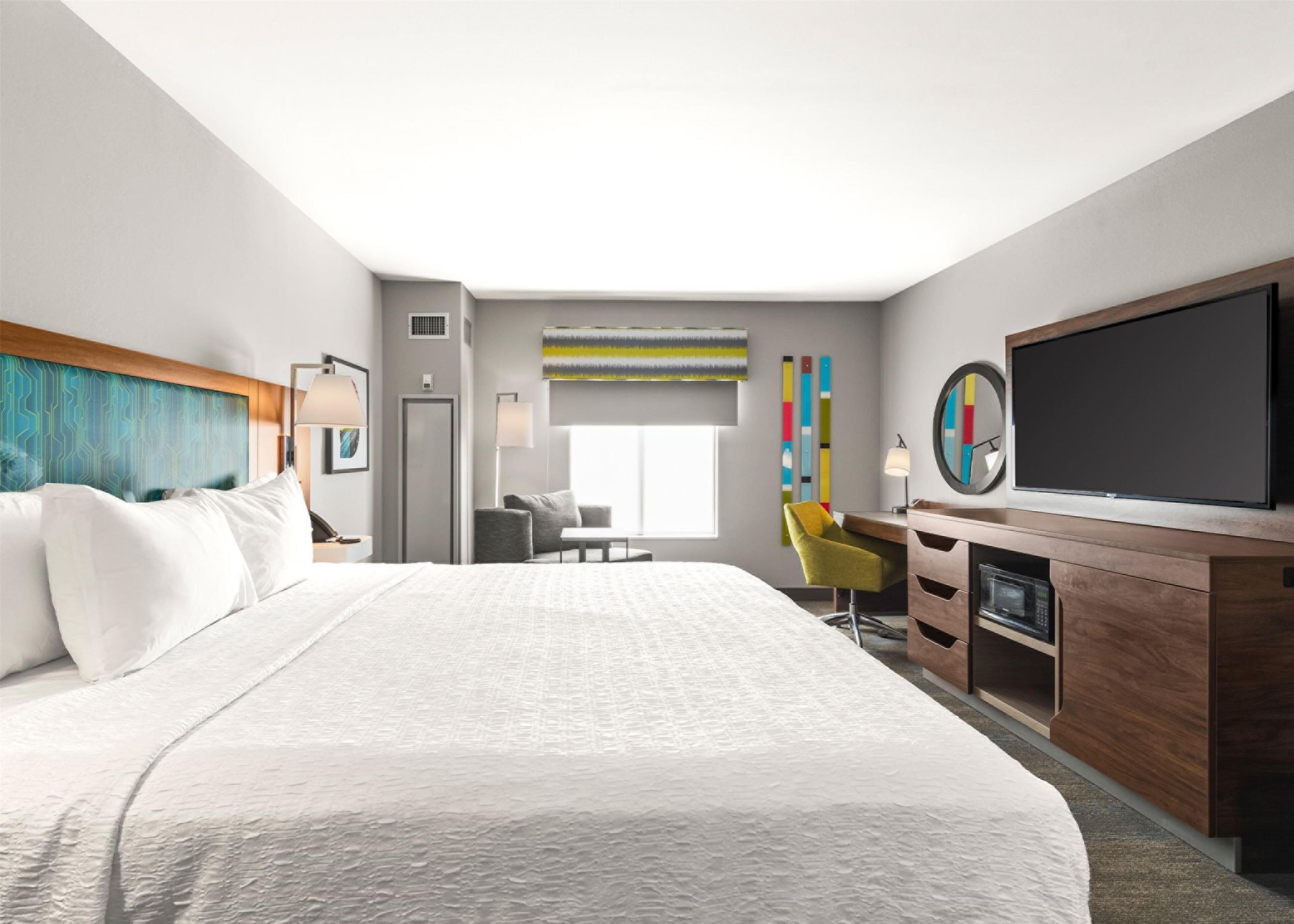 A modern hotel room with a large bed, a desk, a TV, and a window.