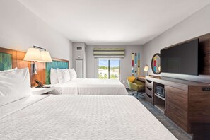 A hotel room with two beds, a TV, a desk with a chair, and a window with a view.