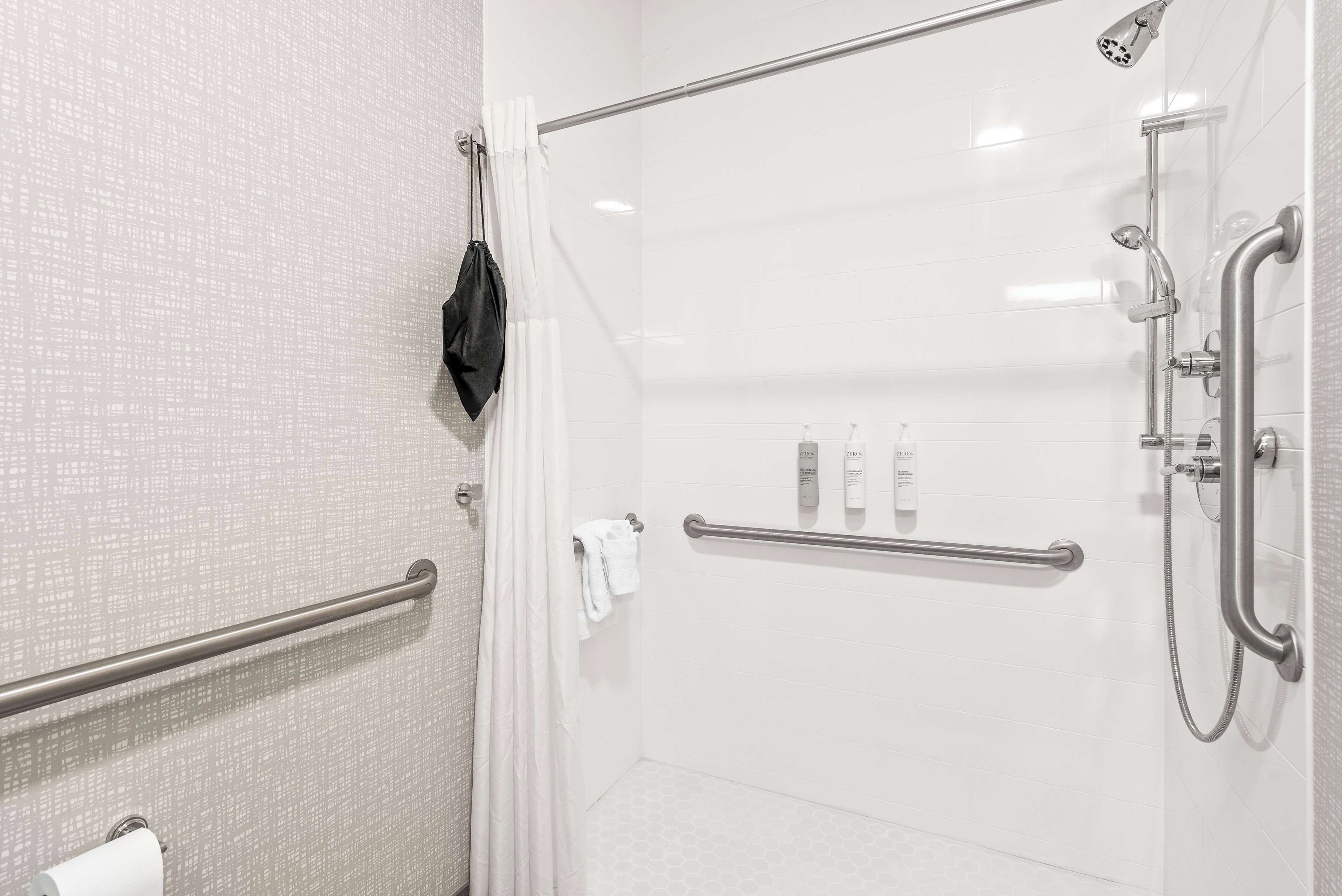A modern shower area with a glass door, a handrail, and a handheld showerhead.