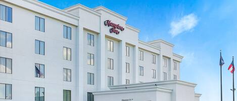 A Hampton Inn hotel with a clear entrance, a sign indicating a 12'7" clearance, and two flags.
