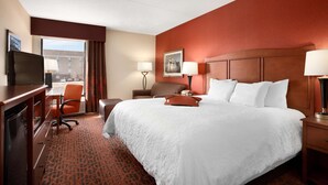 A hotel room with a large bed, a desk with a television, a chair, and a window with curtains. - Hampton Inn Boston/Braintree (Braintree)