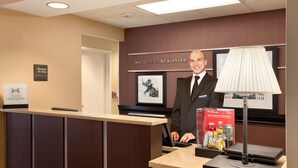 A hotel reception desk with a digital screen, a sign reading "Manager On Duty," and a "Welcome to Braintree" sign. - Hampton Inn Boston/Braintree (Braintree)