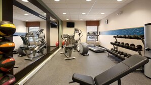 A gym with exercise equipment, a bench, and a wall-mounted mirror. - Hampton Inn Boston/Braintree (Braintree)
