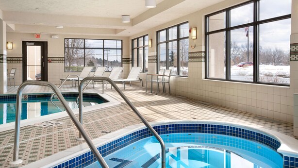 A swimming pool with a tiled deck, lounge chairs, and large windows offering a view of the outdoors. - Hampton Inn Boston/Braintree (Braintree)