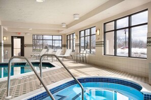A swimming pool with a tiled deck, lounge chairs, and large windows offering a view of the outdoors.