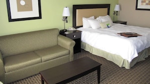 Habitación de hotel con cama, sofá, mesita de noche, lámpara y un cuadro en la pared.