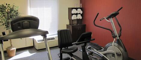 Un gimnasio con una cinta de correr, una elíptica y una bicicleta estática.
