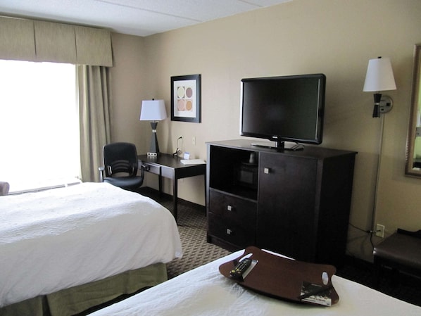 A hotel room with a bed, a desk with a lamp, a television, and a chair.