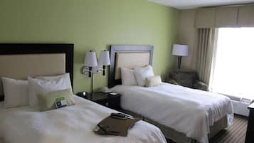 Ein Hotelzimmer mit zwei Betten, einem Nachttisch mit Lampe, einem Sessel und einem Fenster mit Vorhängen.
