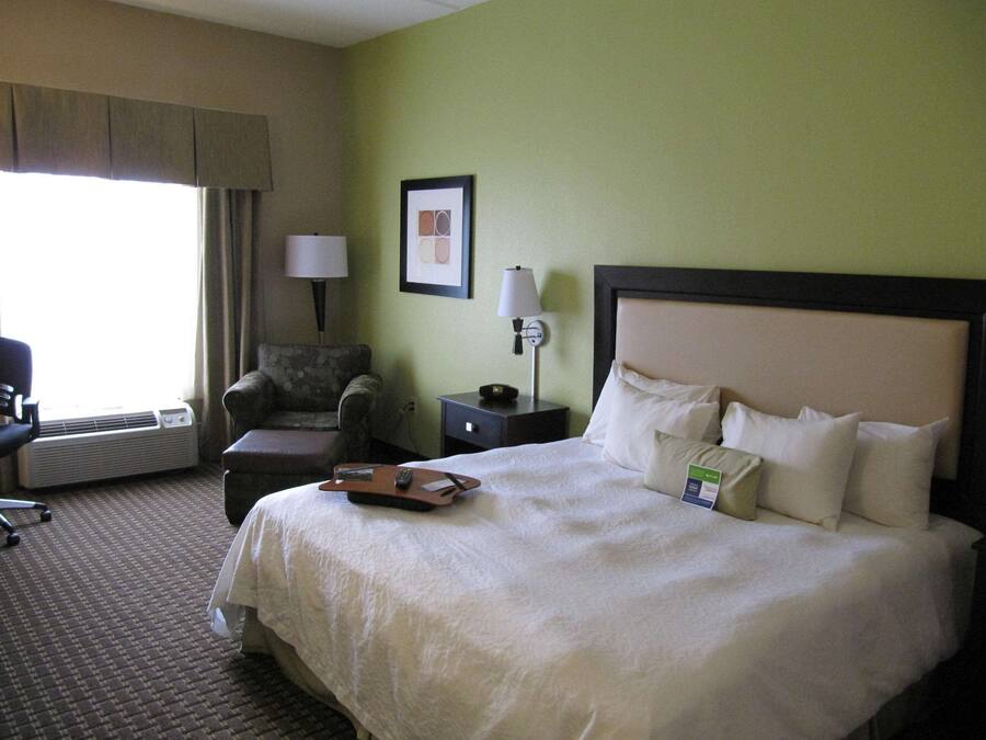 A hotel room with a large bed, a chair, a desk, a lamp, and a picture on the wall.